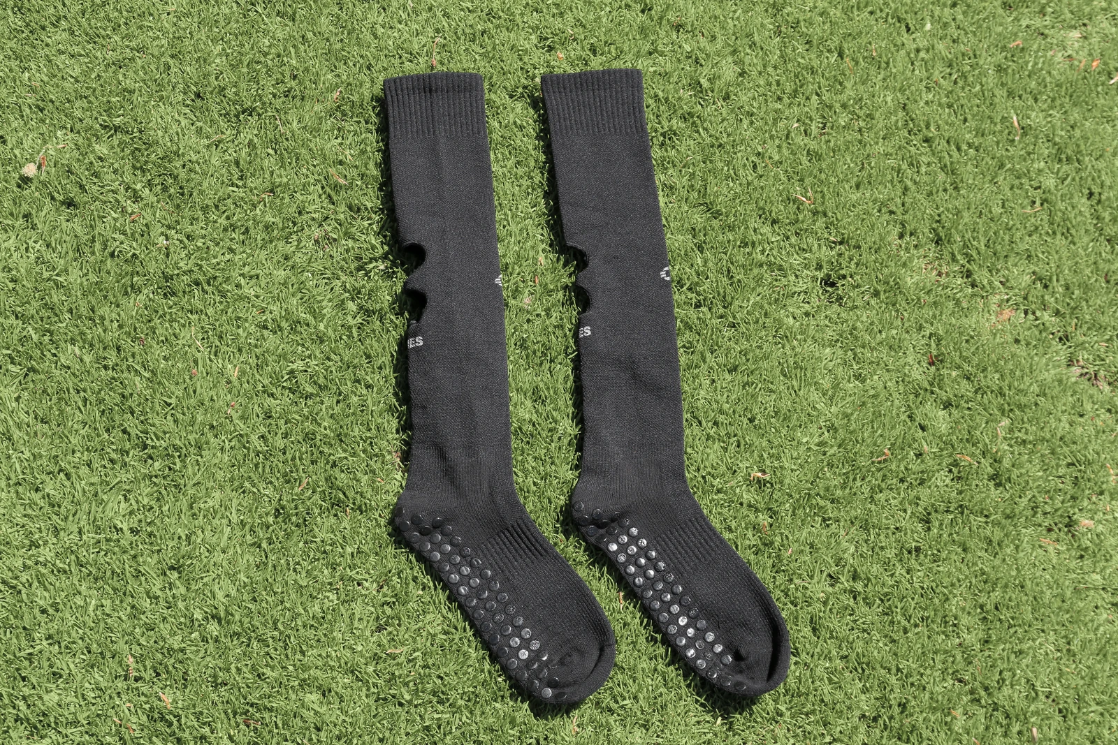 Two black HOLIES Grip Cut Socks on grass, showing the cuff, leg section and foot with grip dots.
