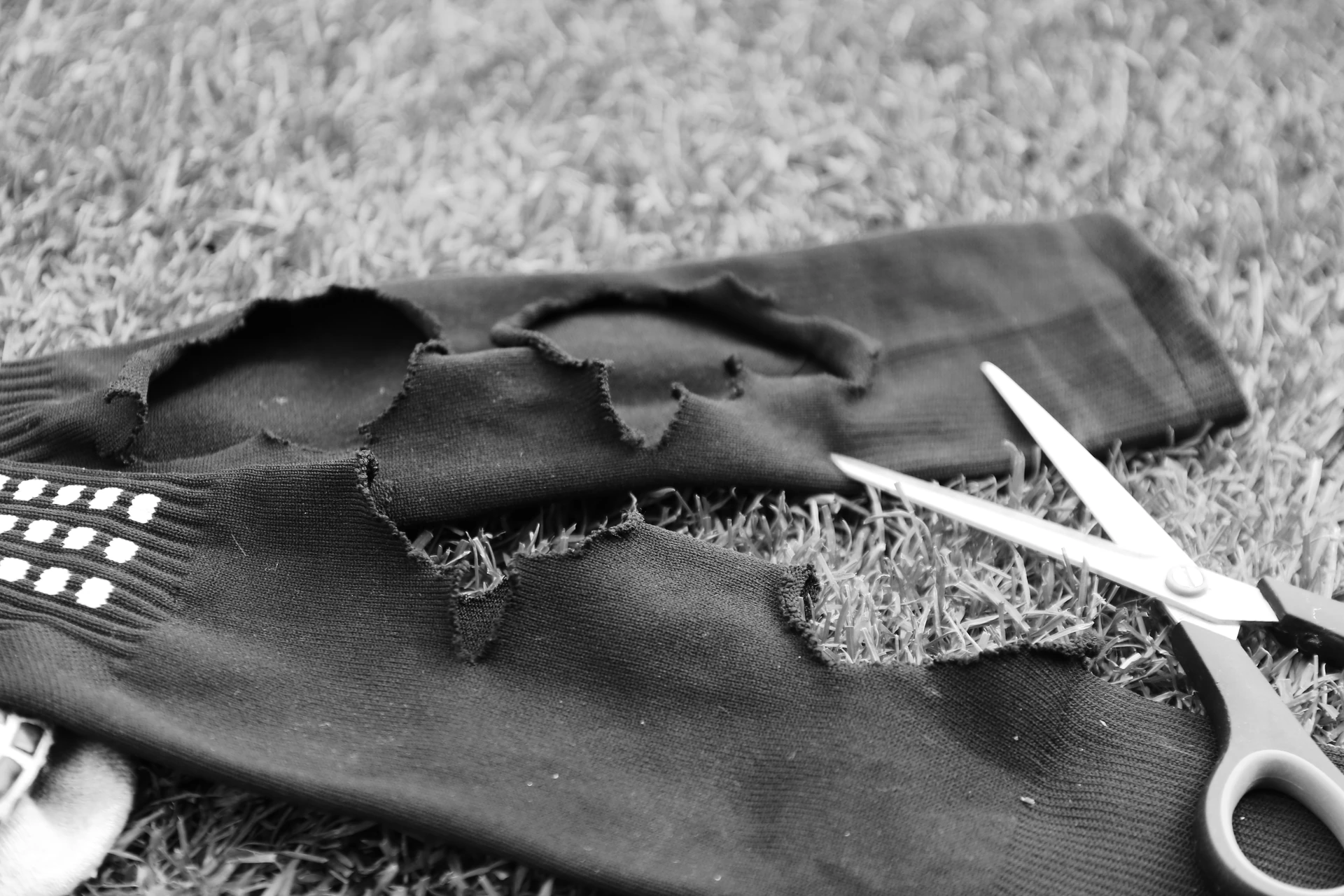 Cut-open black football socks with frayed calf openings and a pair of scissors on grass.