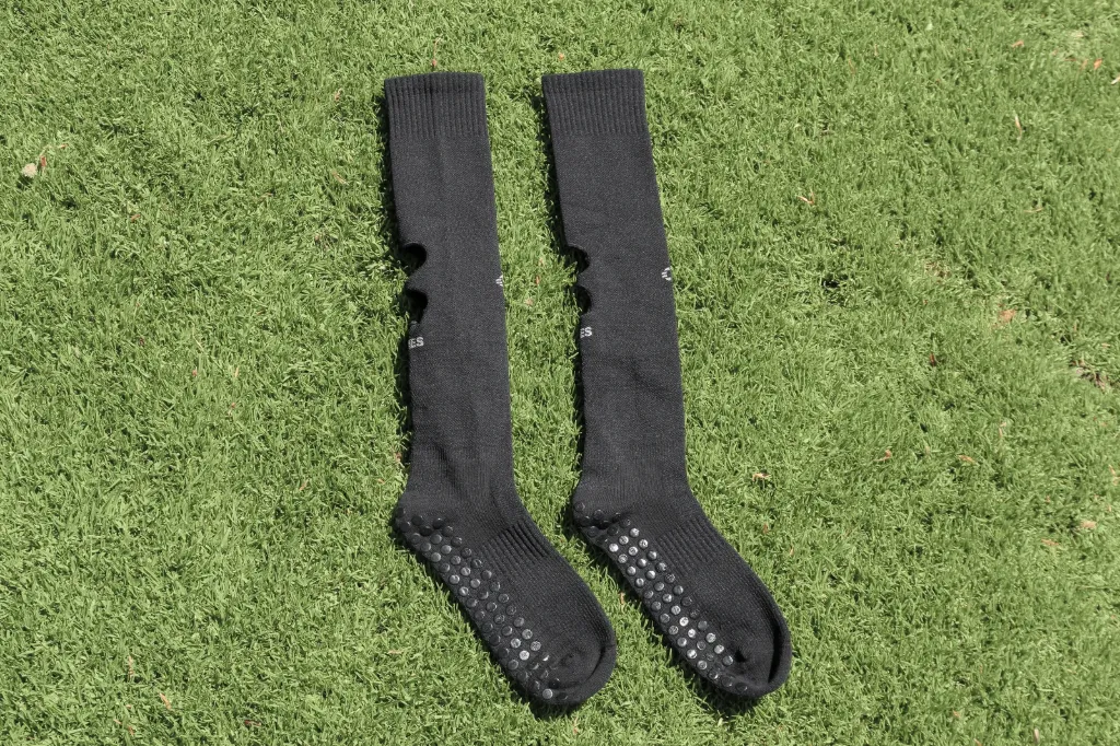 Ein Paar schwarze Grip Cut Socks mit sichtbaren Grip-Sohlen, flach auf Rasen ausgelegt.