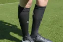Vorderansicht der getragenen schwarzen HOLIES Socken auf dem Fußballplatz.